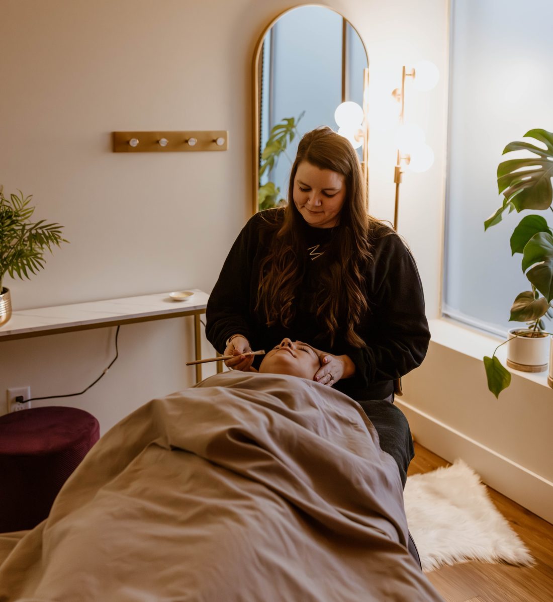 Esthetician performing a facial in a bright treatment room at The Sugaring Hut